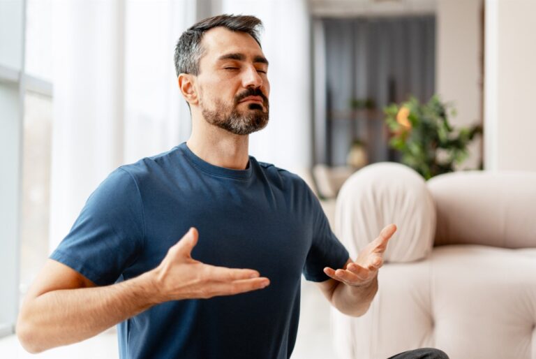 Man in a blue tshirt with his eyes closed, concentrating on his breathing